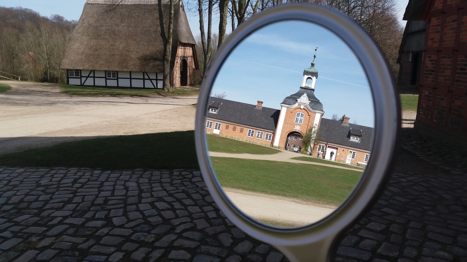 Im Hintegrund ist ein Fachwerkhaus und im Vordergrund die Spiegelung des Einganggebäudes des Museum Molfsee.