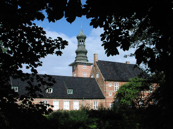 Bachsteingebäude mit Turm, schwharzen Spitzdächern und weißen Fenstern. Umrahmt von Blättern.